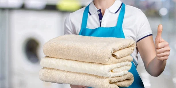 Mujer trabajando en lavandería industrial, sosteniendo toallas y sábanas impecables luego del lavado con ozono.