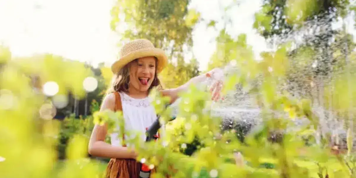 Niña feliz regando el jardín con agua ozonizada para cuidar plantas