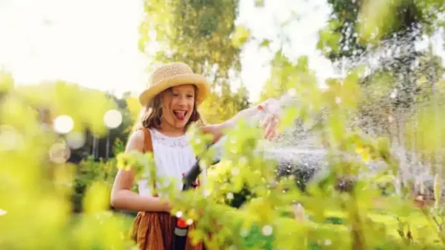 Niña feliz regando el jardín con agua ozonizada para cuidar plantas